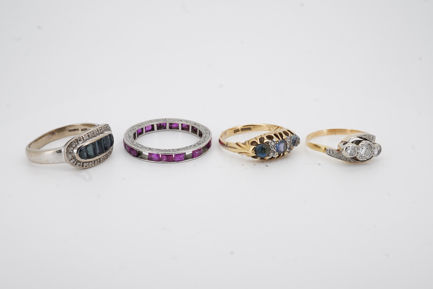 A yellow metal and illusion set three stone diamond crossover ring, size I, an 18ct, sapphire and diamond chip set ring, a modern 18ct gold and six stone sapphire set ring, with diamond chip border and an engraved white